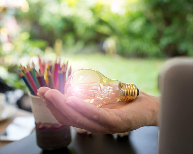 Main tenant une ampoule par dessus une table avec un pot à crayon